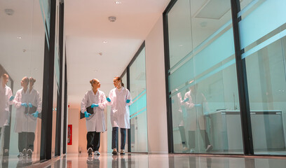 Two scientists in lab coats walk side by side through a sleek laboratory corridor
