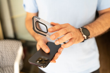 Close-up of a man holding a smartphone and a transparent protective case, preparing to put the case...