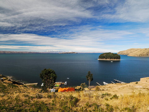 Landscape photography of Isla del Sol on Titicaca Lake in Bolivia. Yellow dry vegetation, deep blue lake, blue sky with gentle white clouds. Colorful boats in harbour.