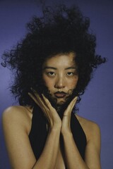 Fototapeta premium Woman with curly hair and dark lipstick posing with hands near face in a modern studio setting.