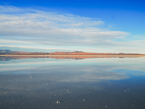 Photography of Salar de Uyuni with mirror effect, picture taken in the middle. of the day, gentle clouds, blue sky, soft light, mountains in the horizon