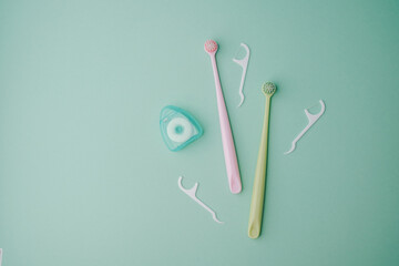 Toothbrush and dental floss container arranged neatly on a light mint background.