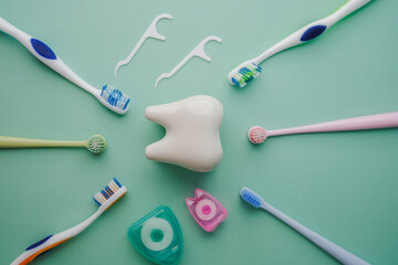 Dental hygiene tools arranged around a large tooth shape on pastel green background