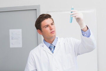 Male laboratory scientist wearing lab coat and latex gloves inspecting blue liquid test tube in lab