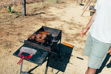 Meat being cooked on a barbecue grill over an open fire in a field. Outdoor cooking, camping, family vacation