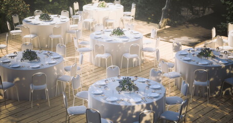 Beautifully arranged tables are set for a special gathering under the soft glow of twilight. Each table is adorned with white linens and floral centerpieces, creating an enchanting atmosphere.