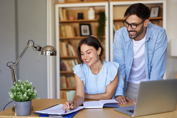 A couple engages in collaborative work at a stylish home office. One partner annotates paperwork, while the other offers support, enhancing their productivity as sunlight streams in.