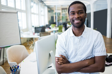 Smiling African American man standing in open-plan office, with monitor and flip chart, copy space