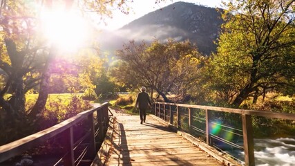 Woman crosses old wood bridge in a golden autumn valley