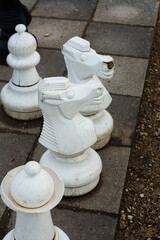 Large white chess pieces on a garden courtyard during a cloudy afternoon, with strategic placements...