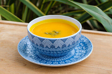 A vibrant bowl of freshly prepared pumpkin soup served in an intricate blue ceramic dish, garnished with seeds. 