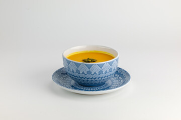 A vibrant bowl of freshly prepared pumpkin soup served in an intricate blue ceramic dish, garnished with seeds. 