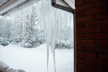 Large icicles hang from the rain gutter of a private house in winter. Risk of breaking and damaging...