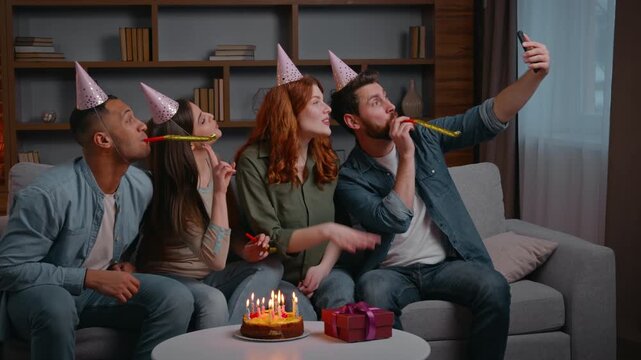 Four multiracial friends at home birthday party make selfie photo together happy smiling diverse men women people buddies in festive hats recording vlog video on mobile phone posing celebrate event