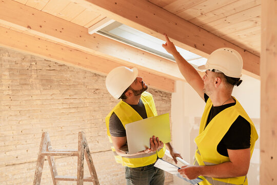 Two male Construction workers using laptop inspecting wooden beams in building renovation project