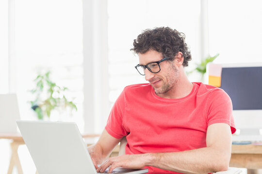 Typing middle-aged man working on silver laptop at bright office desk with potted plant, copy space - Powered by Adobe
