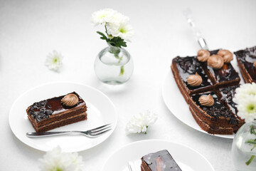 Rich chocolate cake slices with cream and flowers on a white table