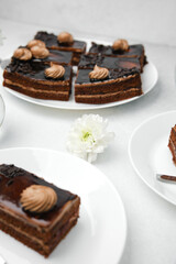 Delicious chocolate cake slices layered with cream and topped with frosting on plates with white flower