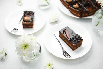 Delicious chocolate layer cake on white plate with fork and white flowers