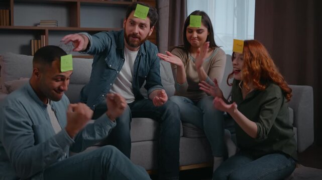 Four diverse friends multiracial people playing guessing game with sticky notes on forehead quess personage word Latina man win buddies applauding laughing together play charades funny entertainment