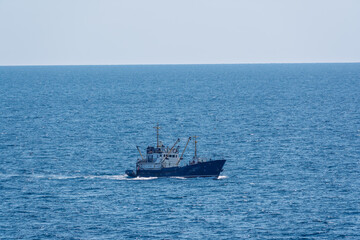 Fishing boat in blue sea and clear sky with birds flying overhead.