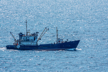 Fishing boat in blue sea and clear sky with birds flying overhead.