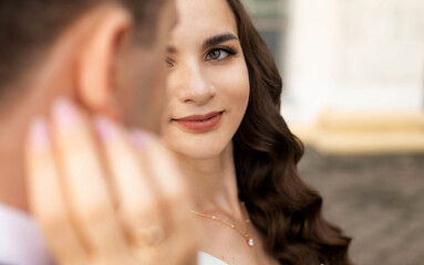 A bride and groom are standing and looking at each other. The man is wearing a suit and tie, and...