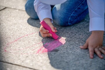 Child drawing with pink chalk on pavement.