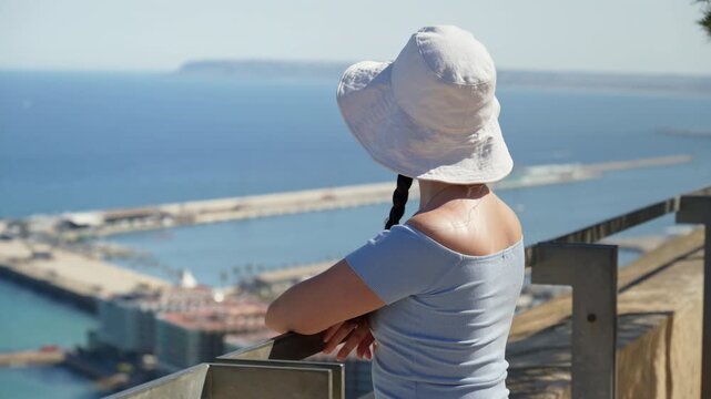 A traveler girl in a white bucket hat takes in the coast from a breezy hilltop lookout in Alicante, Spain
