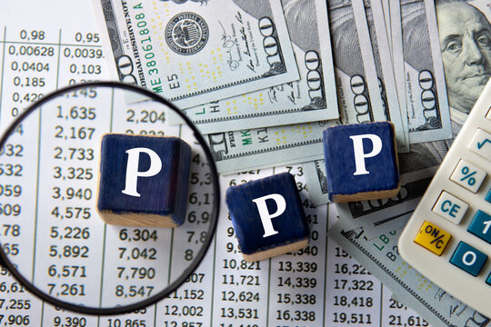 PPP - acronym on wooden cubes against the background of banknotes and calculator