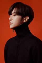 Profile portrait of a young Asian man in a black high-neck sweater against a red background.