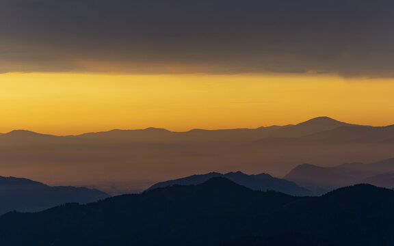 View of the majestic mountain ranges silhouetted against a vibrant gradient sky of orange and purple hues, creating a tranquil vista, Styria, Austria.