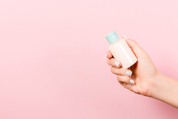 Female hand holding cream bottle of lotion isolated. Girl give tube cosmetic products on pink background