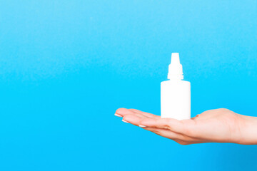 Female hands hold medicine bottle nose spray on blue background isolation