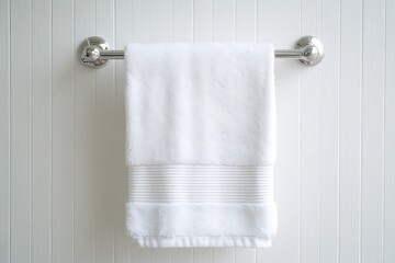 A pristine white bath towel hangs neatly on a chrome towel bar against a white paneled wall