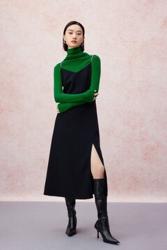 Confident woman in a stylish black dress and green turtleneck, striking a pose.