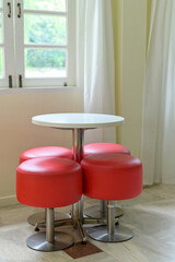 Vibrant red stool set with white round table offers modern furniture design for an indoor space. compact seating by bright window feels cheerful and inviting