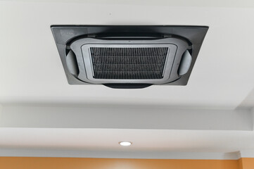 Fototapeta premium Black cassette air conditioner on white ceiling provides cool comfort. modern cooling ventilation hvac system controls climate in an office or home interior