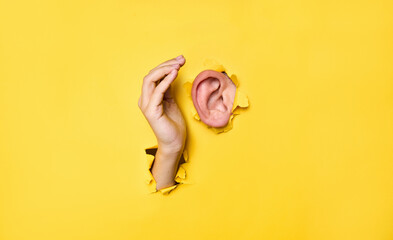 Close-up of  human ear and hand through torn yellow paper