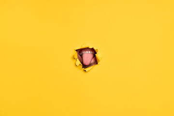 Close-up of human showing tongue through torn yellow paper