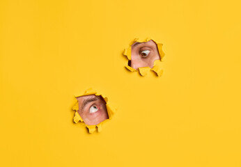 Human eyes peeking through yellow paper to each other