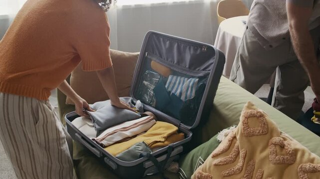Young couple packing suitcase at home, man handing neatly folded clothes to his girlfriend as they preparing for vacation together