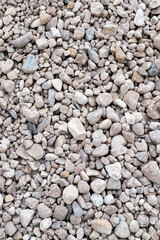 Textured surface of small gravel stones in various shades of gray and beige, creating a natural texture for landscaping, construction, or decorative purposes. Vertical background with copy space