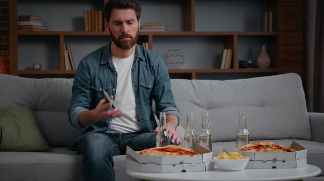 Lonely Caucasian man calling friends talking mobile phone inviting to home party canceled invitation with pizza chips alone single middle-aged male guy on couch without no friends birthday isolation