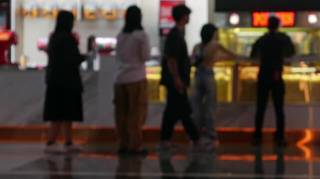 Blurred cinema concession stand with customers buying popcorn and drinks under colorful neon lighting at movie theater