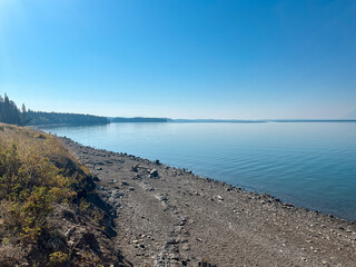 Calm Jackson Lake with rocky shoreline and Grand Teton mountains under a clear blue sky.
