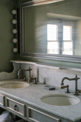 Vintage double sink bathroom vanity with marble countertop, antique brass faucets, and a large wall mirror. Soft natural light creates a calm and rustic atmosphere.