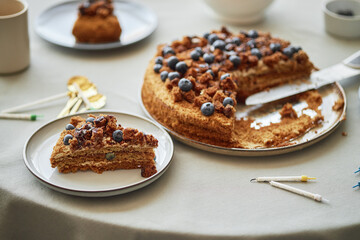 Homemade layered cake with blueberries and crumbled topping sitting on table, one slice served on...