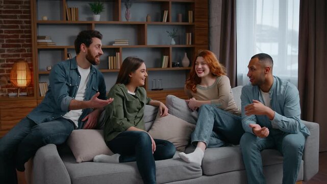 Four diversity friends on party in living room talking communicate weekend at home spending time together multiracial women girls men guys smiling talk conversation friendship sharing news friendly
