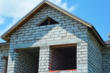 The facade of the unfinished house with walls made of aerated concrete, attic window, a metal roof without soffits and without a gutter.